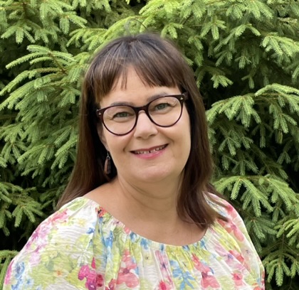 Maarit Karhula, erikostutkija Kelan tutkimus. Kuvassa Maarit hymyilee kesällä pensaan edessä.